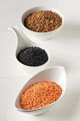 Different assorted lentils mix with red, brown and black beluga lentils in white bowls on white wooden table background