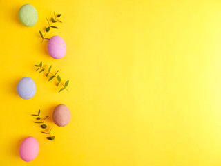 Flat lay composition of Happy Easter holiday concept. Colorful pastel egg with eucalyptus branch on yellow background. Copyspace, top view.