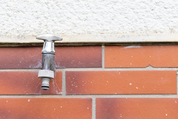 Old silver faucet for water on the wall of an old house outside in the garden