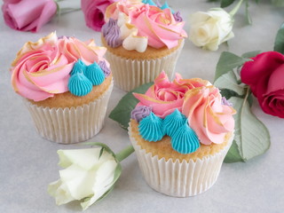 Three cupcakes with beautiful frosting among some roses on a tabletop
