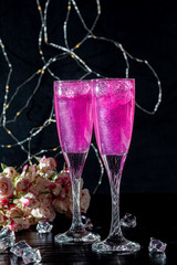 Sparkling brilliant raspberry drink. Champagne in two glasses stands on a wooden table with ice....