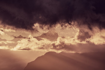 Alpine mountain surrounded by clouds and sunlight