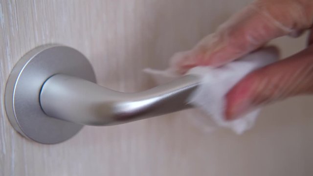 A hand wearing disposable rubber glove cleans door handle by alcohol slice