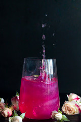 A sparkling brilliant raspberry drink in a glass stands on a wooden table with ice. In the...
