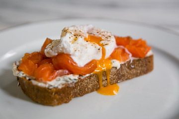 Bruschetta with salted red fish and poached egg dripping down on a white plate