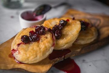 Three fried cheesecakes on a wooden board with cherry jam on top