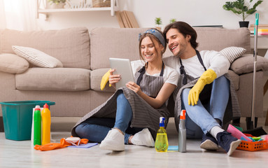 Smiling couple relaxing with digital tablet on floor after spring-cleaning apartment