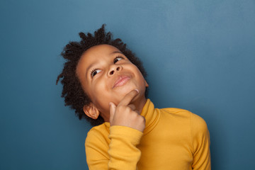 Small black child boy thinking and looking up on blue background © millaf (Nemchinova)