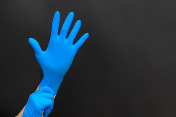 Female hands in blue medical protective gloves. Doctor, surgeon or nurse. Means of protection against germs and dirt. Black background, copy space.