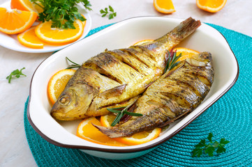 Baked roach fish with vegetables and oranges in a ceramic bowl. Diet menu
