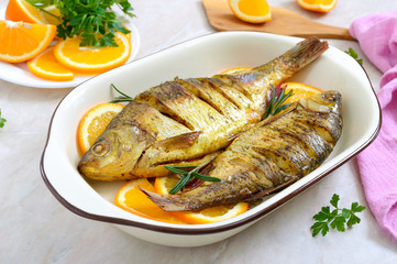 Baked roach fish with vegetables and oranges in a ceramic bowl. Diet menu