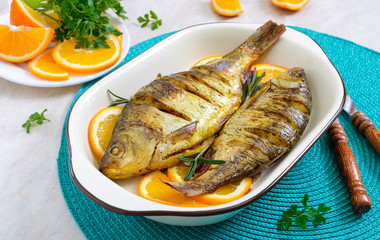 Baked roach fish with vegetables and oranges in a ceramic bowl. Diet menu