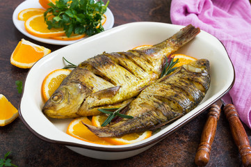 Baked roach fish with vegetables and oranges in a ceramic bowl. Diet menu.