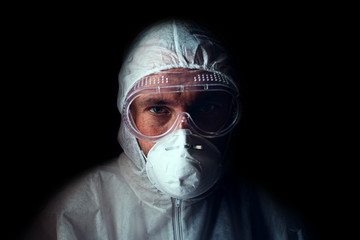 A doctor with a tired look in a respirator, glasses and a bacteriological protection suit. Low key....