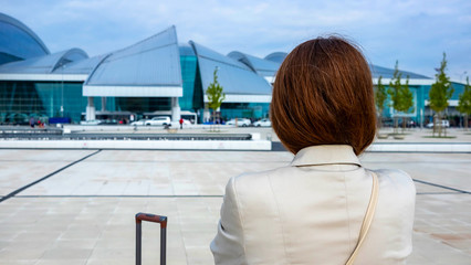 Rostov-on-Don,Russia - April 29,2018: rear view Girl. looks at the airport before traveling, getting ready to board the plane. next to it is the handle of the suitcase. her baggage