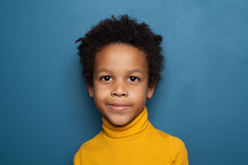 Curious black child boy smiling on blue background