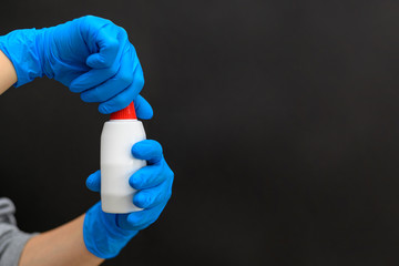 Female hands in blue medical gloves hold a white jar with a red closed lid. Antiseptic, drops or lotion. Medical kit. Copy space. Horizontal view, dark background.