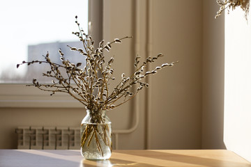a bouquet of willow branches in a vase wrapped in red paper on a wooden table in the kitchen in the sunlight in brown tones © Elena