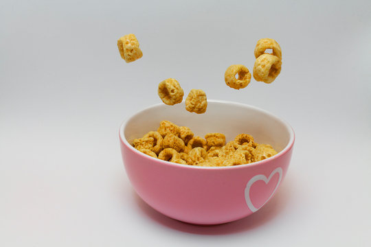 snack de aros de maiz cayendo en un bol rosa con corazon sobre un fondo blanco