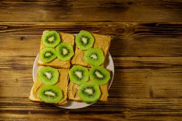 Tasty sandwiches with peanut butter and kiwi fruits on wooden table. Top view