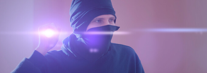 close up bandit thief in the mask with a torch light while making a crime wide banner panorama