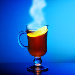 Cup of hot steaming tea with lemon on a blue background