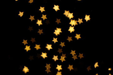Blurred view of star shaped lights on black background. Bokeh effect
