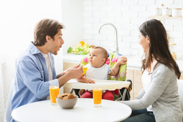 Obraz na płótnie Canvas Young parents feeding baby son at kitchen, free space