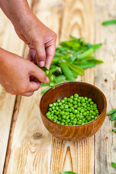 closeup of woman hand depod green peas in brown dish, on wooden table.