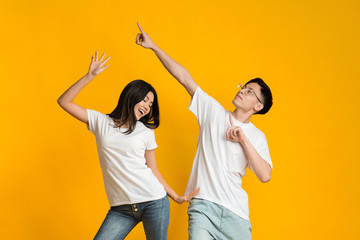 Emotional asian guy and girl dancing over yellow background