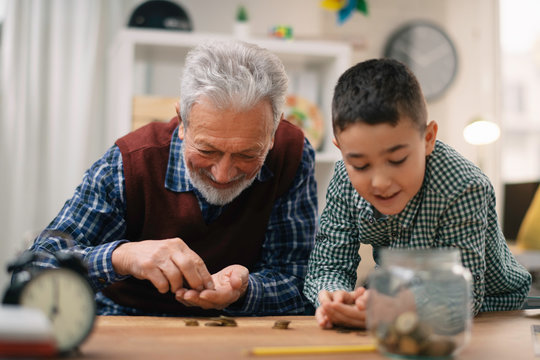 Grandpa and grandson saving money. Grandfather teaching grandchild how to save money.