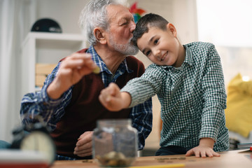 Grandpa and grandson saving money. Grandfather teaching grandchild how to save money.