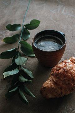 Cappuccino coffee and croissant on wooden background on the table. Perfect breakfast in the morning. Rustic candid style.