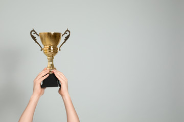 Man holding gold trophy cup on light grey background, closeup. Space for text