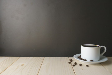 Fototapeta na wymiar coffee cup with beans on wooden desk against dark background. copy space for your text