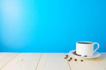 coffee cup with beans on wooden desk against blue background. copy space for your text