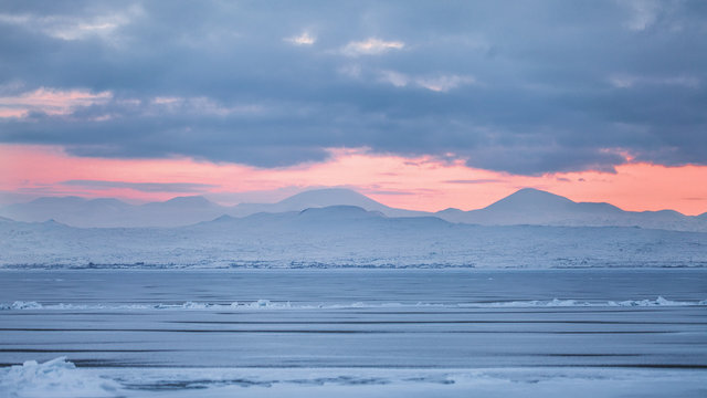 Natural wonderful background from frozen lake Sevan in Armenia , Sunrise makes beautiful warm golden light background between blue clouds and mountains
