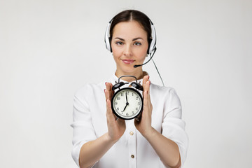 Beautiful smiling woman consultant of call center in headphones holding alarm clock on gray...