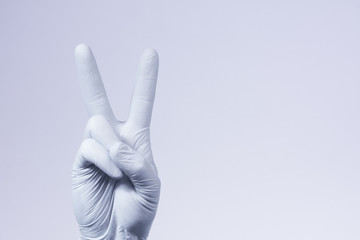 V sign is showed by right man hand in a white medical glove on a white background. The symbol of Victory. Victory over a virus.