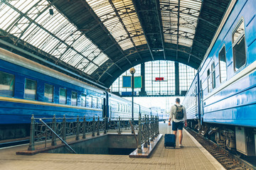 man walking with suitcase on wheel by railway station