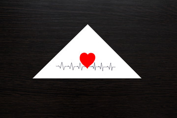 Triangular white envelope on the background of a wooden table. The envelope has a red heart and pulse drawn on it .