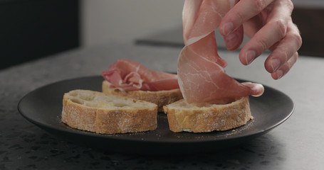 man hand put prosciutto on ciabatta slices black plate