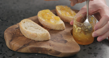 man spreading orange marmalade on ciabatta slices on wood board