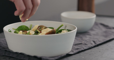 man adding cheese chunks to salad with kumato tomatoes and spinach in white bowl