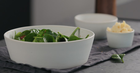 kumato tomatoes to fresh spinach leaves into white bowl to make a salad
