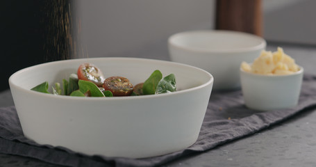 man seasoning salad with kumato tomatoes and spinach in white bowl