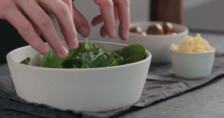 man add fresh spinach leaves into white bowl to make a salad