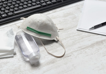 hydro alcoholic gel , dust mask gloves and handkerchiefs on a desk with keyboard