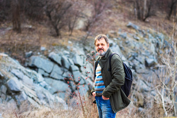 A middle-aged bearded man with a dark backpack stands on the shore of a flooded quarry.