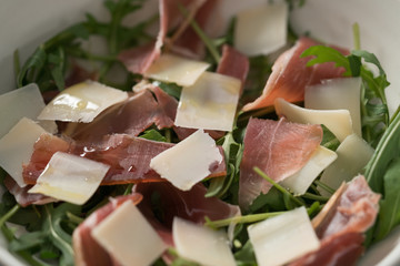 Salad with prosciutto, parmesan and arugula in white bowl closeup